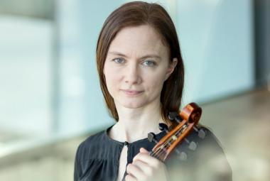 Kuvassa on Maija Lampela puolivartalokuvassa ja hännellä on viulu kädessään. Hän on pukeutunut murtaan  puseroon. Taustalla on vaalean sinistä seinää.