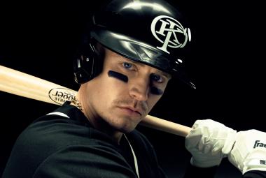 Kuvassa on puolivartalokuvassa Gettomasa mustassa kypärässä ja hän pitää olkapäällään vaaleaa pesäpallomailaa. Hänellä on musta pusero päällään ja tausta on musta.