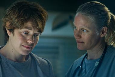 Kuvassa ovat vasemmalla puolivartalokuvassa Oona Airola ja oikealla Laura Birn himmeässä valossa. Molemmat katsovat alaspäin.