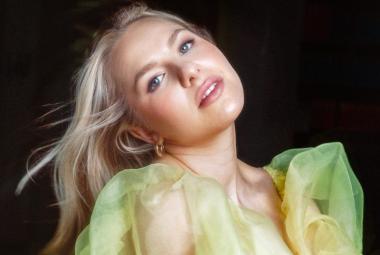 Kuvassa on Ilta puolivartalokuvassa ja hänellä on pää taivutettuna vasemmalle.  Vaaleat hiukset lentävät vasemmalle. Hänellä on päällään vaalean vihreä sifonkinen mekko.