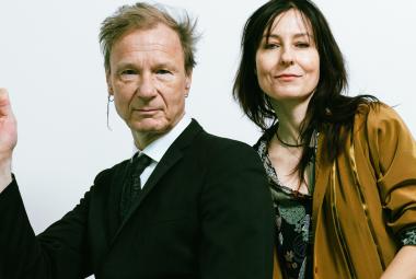 Kuvassa on vasemmalla Ismo Alanko puolivartalokuvassa mustassa takissa. Hänellä on oikea käsi nostettuna sivulle. Oikealla on Mariska ruskeassa villa takissa ja harmaassa puserossa.