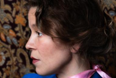 Kuvassa on Viivi Prokofjev sivukuvassa. Hänellä on surkeat kiharat hiukset. Taustalla on ruskean kirjavaa tapettia.