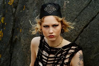 Kuvassa on Vilma Jää puolivartalokuvassa. Hänellä musta, hihaton löyhä verkkopaita päällään ja musta päähine päässään. Taustalla on tummaa kalliota.