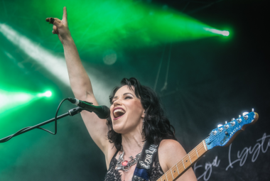 Kuvassa on Erja Lyytinen kuvattuna alaviistosta ylöspäin ja hän on laulamassa mikki edessään. Hänellä on oikea käsi pystyssä ja päällään hihaton pusero sekä kitara kädessään. Taustalta tulee vihreää valoa.