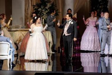 Kuvassa on pitkissä, leveä helmaisissa puvuissa ja frakeissa juhlivia ihmisiä ja he nostelevat maljoja seisoessaan.  