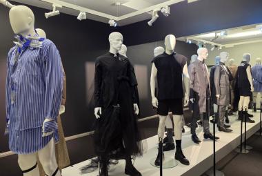 Kuvassa on miesmallinukkeja ja vasemmalla on sinipaitainen mallinukke.  Muut ovat rivissä mustissa ja ruskehtavissa väreissä. 