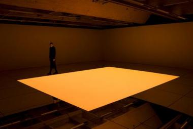 Kuvassa on ruskeassa tilassa kelluva, hiukan kaareva neliömäinen oranssi laatta.