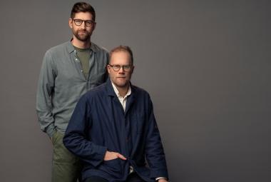 Kuvassa ovat Lars Berge seisomassa harmaassa puserossa Axel Gords Humlesjön takana ja Humlesjö istuu. Hänellä on musta pusero ja pitkät housut. Tausta on tumman harmaa.