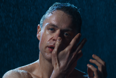 Kuvassa on puolivartalokuvassa miehen alaston yläosa ja hän on hikinen. Mies pitää oikeaa kämmentä poskellaan. Tausta on tumma.