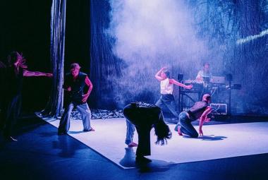 Kuvassa on sinisellä valolla valaistulla näyttämöllä neljä tanssijaa erilaisissa asennoissa. Heillä  on farkkuhouut ja eerilaisia paitoja. Keskellä on vaaleaa savua.