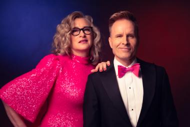 Kuvassa on vasemmalla Katja Ståhl pinkissä, glittermekossa, jossa on leveä hihat. Hän pitää vasenta kättään Mikko Kekäläisen olkapäällä, jolla on musta takki, valkoinen paita ja pinkki rusetti. He ovat puolivartalokuvassa. Tausta on tummansininen.