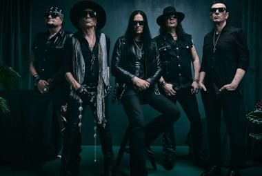 Kuvassa on viisi yhtyeen jäsentä seisomassa ja heillä on mustat vaatteet päällään. Kuvan sävy on tumma.