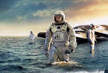 Kuvassa on keskellä vaaleassa avaruuspuvussa ja kahlaa vedessä. Taaempana kahlaa toinen avaruuspukuinen henkilö. Takana on vedessä on litteä alus ja sen edessä on kolmas henkilö. Yllä on tumman sinistä pilveä, joka heijastuu tumman siniseen veteen