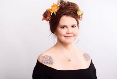 Kuvassa on Katja Kettu puolivartalokuvassa.  Hänellä on mustassa mekossaan avonainen kaula-aukko ja oikean olkaimen ruusutatuointi näkyy.  Päässään hänellä punaisissa hiuksissaan oransseja ja ruskehtavia kukkia. Tausta on vaalea.