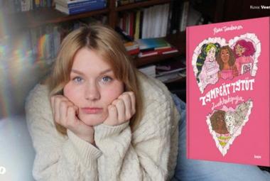 Kuvassa on Riina Tanskanen löhöämässä eteenpäin ja hän nojaa poskiinsa. Hänellä on vaalea villapaita päällään. Oikealla on kuva kirjan kannesta, joka on vaalean punainen. Takana on kirjahyllyä.