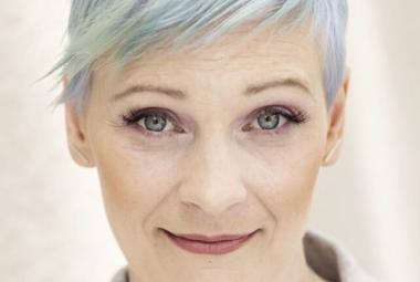  Kuvassa on Annukka Salama kasvokuvassa ja hänellä on sinertää lyhyissä hiuksissaan. Tausta on vaalea.