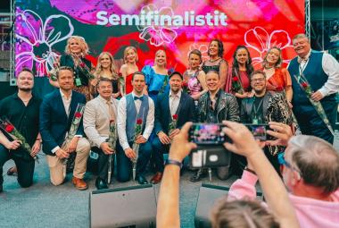 Kuvassa ovat kahdessa rivissä Tangomarkkinoiden semifinalistit ja heistä ensimmäisessä rivissä olevat nojaavat toiseen polveensa. Taustalla on punaisia kukkia Tangomarkkinoiden isossa lakanassa. Edessä on yleisöä ottamassa valokuvia.