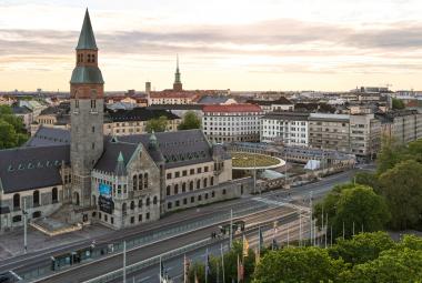 Kuvassa on Kansallismuseo ja sen ympäristö ilmasta käsin. Museo on harmaasta kivestä ja siinä on harmaa torni, jossa on puna-musta huippu. Taustalla on valkoisia taloja. Edessä on Mannerheimintie.