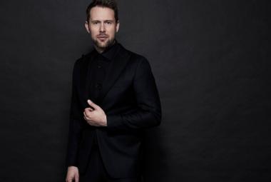 Kuvassa on Waltteri Torikka seisomassa mustissa vaatteissa ja tausta on tumma.