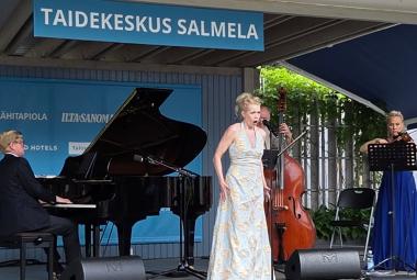 Kuvasswa on Kuvassa on vasemmalla Janne Hovi soittamassa flyygeliä ja keskellä Helena Juntunen vaaleassa, pitkässä puvussa laulamassa. Takana soittaa kontrabassoa Hannu Rantanen takana ja oikealla Maija Linkola viulua pitkässä, sinisessä puvussa. Päällä lukee Taidekeskus Salmela.