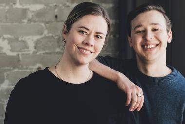 Kuvassa on vasemmalla Lotta Fors ja oikealla Jakob Norrgård. Hän pitää oikeata kättään Lotta Forsin olkapäällä. Heillä molemmilla on mustat t-paidat päällään.  Taustalla on harmaan valkeaa tiiliseinää.
