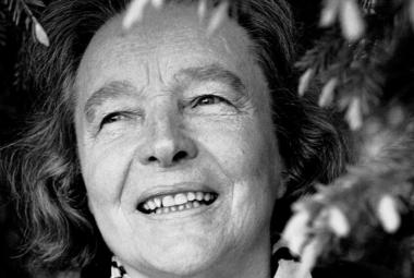 Kuvassa on Eeva Kilpi kasvokuvassa ja hänen ympärillään on kuusenoksia ja jouluvaloketjua. Kuva on musta-valkoinen.