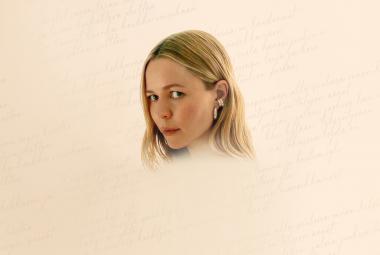 Kuvassa on Paula Vesala kasvokuvassa ja hänellä on vaaleahkot, pitkät hiukset. Kasvot ovat keskellä vaaleaa taustaa.